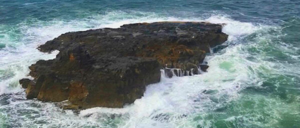 Powerful waves crashing against a strong rock, symbolising mental toughness and resilience under pressure.