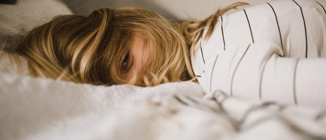 Exhausted woman lying in bed, showing signs of burnout and emotional fatigue.
