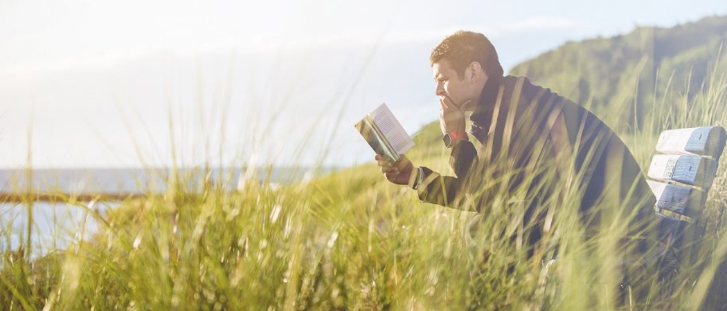 Man sitting quietly by the coast reading a book, enjoying the calming effects of solitude and nature.