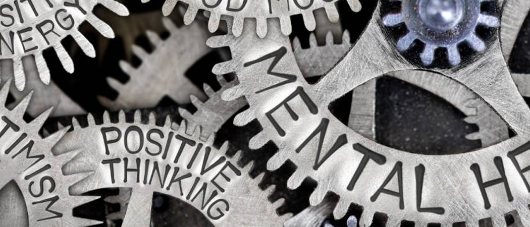 Close-up of interlocking metal cogs engraved with words like mental wellbeing, positive thinking, and resilience.