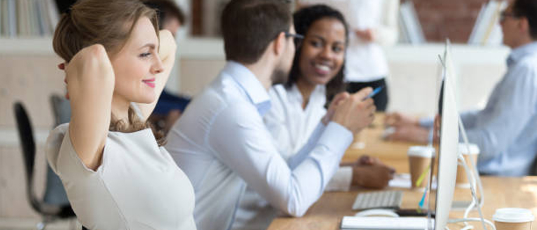A relaxed female office worker smiling with satisfaction while her colleagues engage in a casual conversation in the background, symbolising a healthy and balanced work environment.