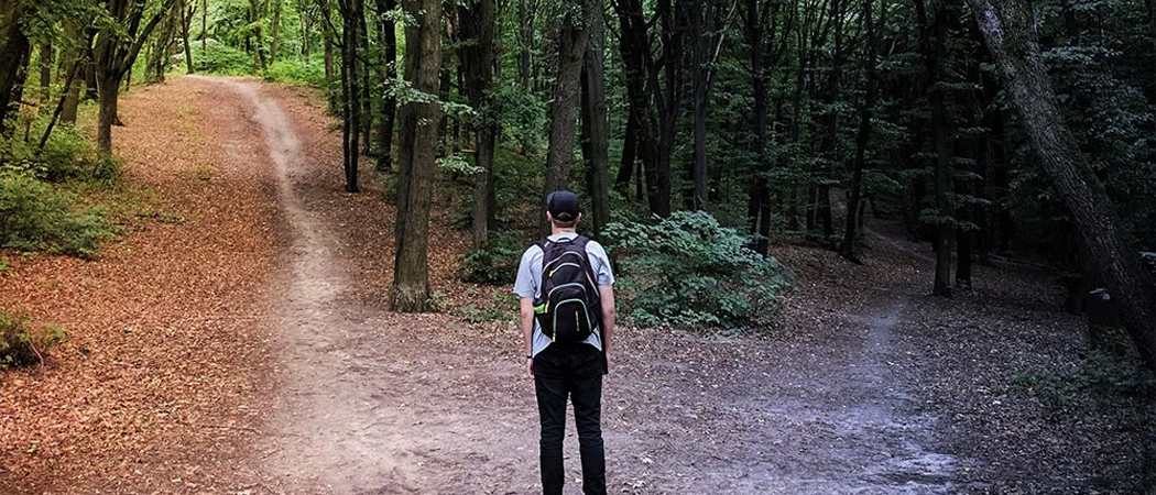 Man at a crossroads in nature, uncertain which path to choose