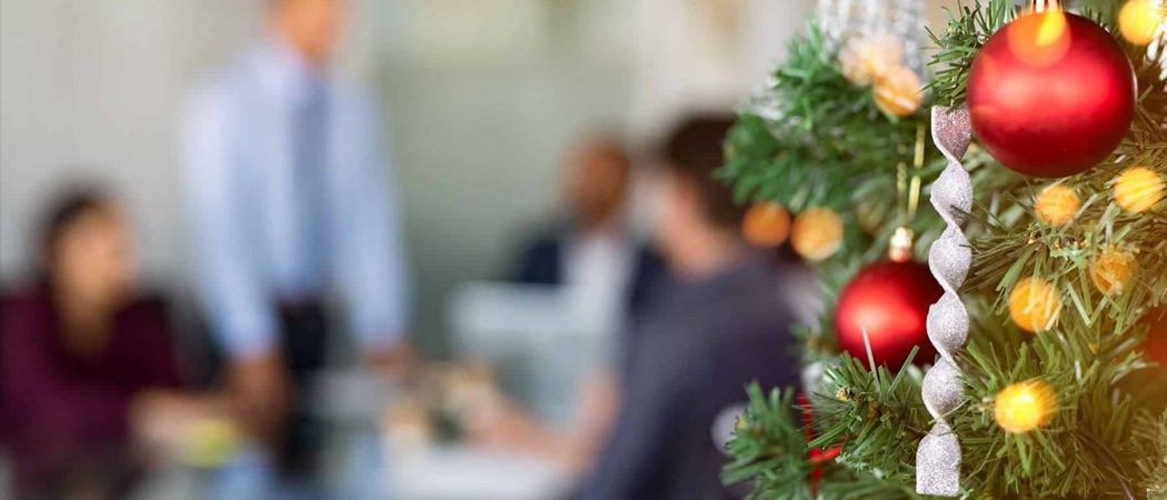 Close-up of a Christmas tree in a modern office with blurred coworkers in the background, symbolising festive season workplace wellbeing.