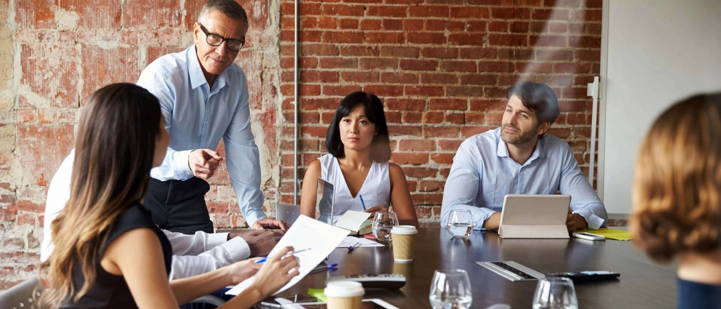 A group of leaders and stakeholders seated around a conference table, collaborating on workplace strategy.