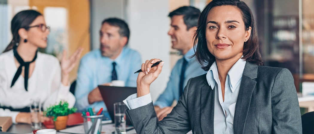 A professional business leader in a modern office engaged in a collaborative discussion with their team, demonstrating psychological safety and capable leadership.