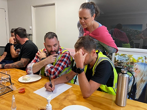 A Get Mentally Fit facilitator guiding team members in high-visibility vests through a manager wellbeing exercise around a wooden table.