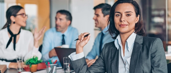A diverse and professional team of five people stands together in a bright, modern office with a city view. They are smiling and looking confidently toward the camera, representing a unified, capable, and mentally fit leadership team that embodies psychological safety and collective strength.