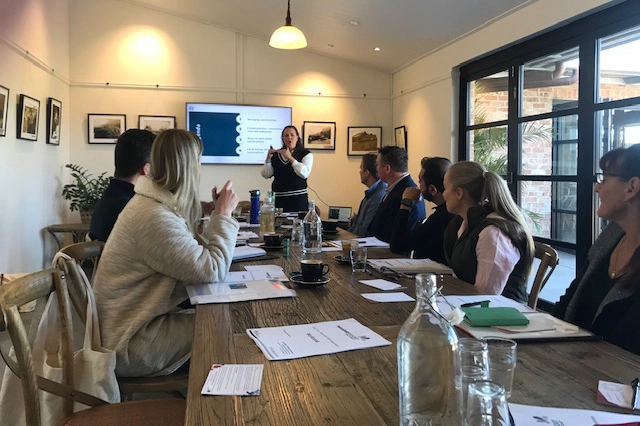 Get Mentally Fit facilitator leading a leadership development workshop with professionals gathered around a boardroom table.