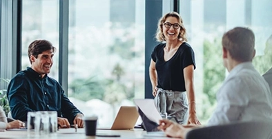 A female leader smiling and leaning on a boardroom table during a Get Mentally Fit leader support session.
