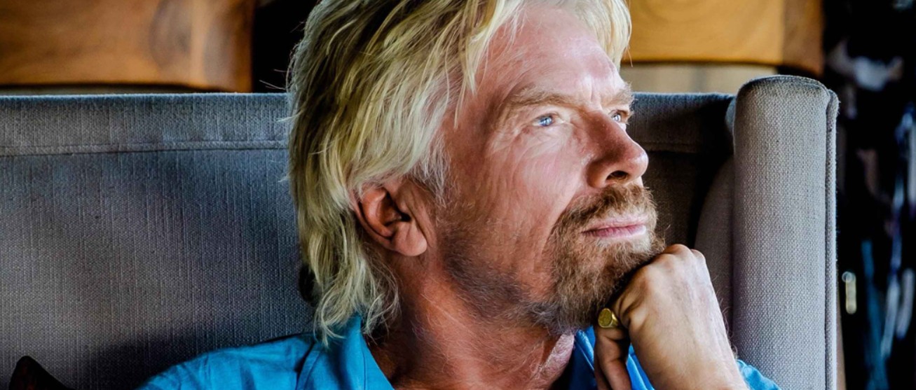 A close-up profile portrait of Sir Richard Branson resting his chin on his hand, looking upward thoughtfully with a focused and contemplative expression while sitting in an armchair.