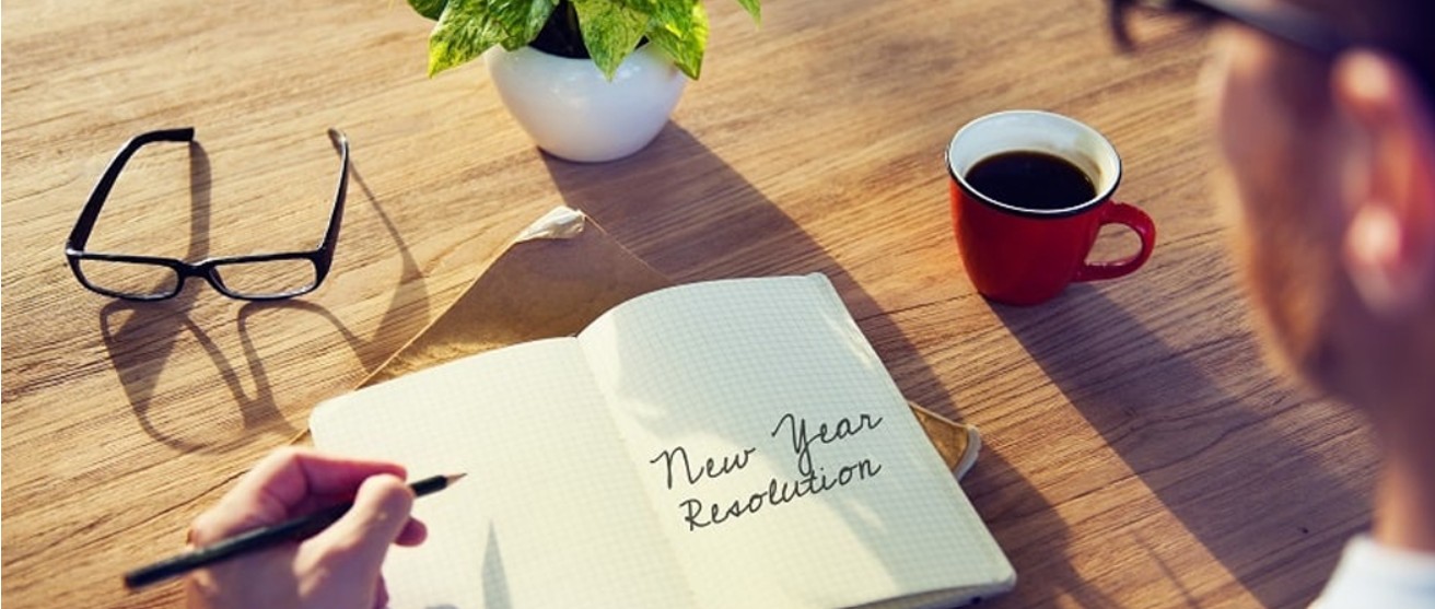 Open diary on a wooden table with “New Year Resolution” written on the page in cursive.