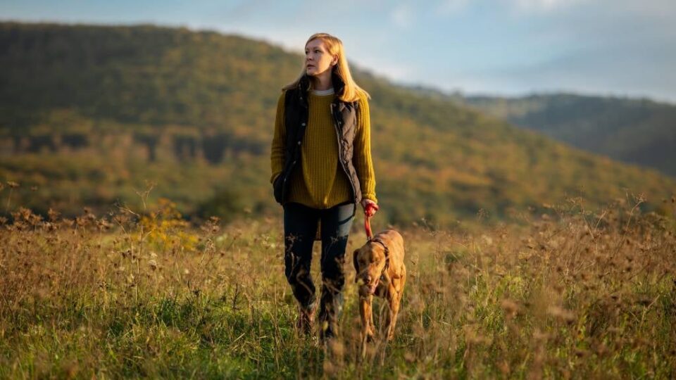A woman walking her dog in a quiet natural setting, appearing calm and thoughtful, using the time for personal reflection. 3 powerful reasons to reflect.