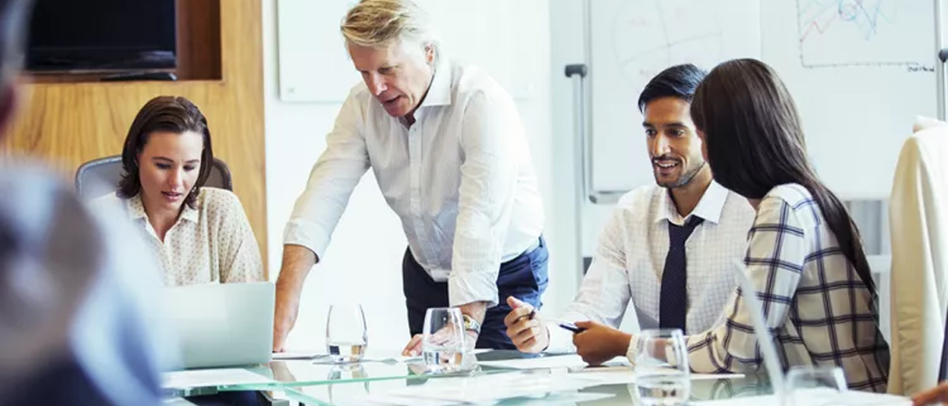 Professional team collaborating in a boardroom while a confident leader stands to guide the discussion.